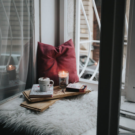 Lap board in a urban window sill with candle, books, and coffee mug on it.